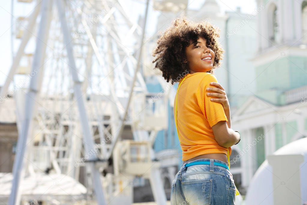 Curly-haired girl hugging herself during sightseeing