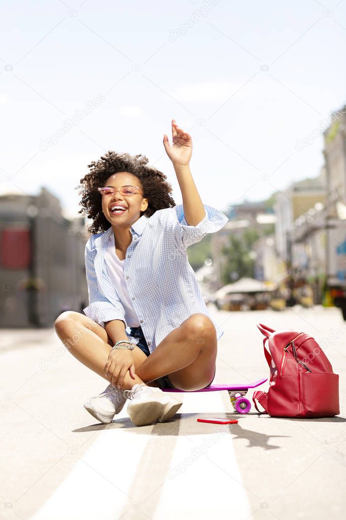 Joyful woman calling someone while sitting on skateboard