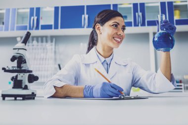 Esmer kimyager holding ampul mavi sıvı ile gülümseyen
