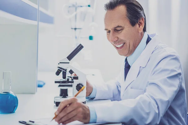 Químico radiante haciendo notas sentado a la mesa — Foto de Stock