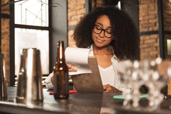 Pretty curly woman looking through menu at pub