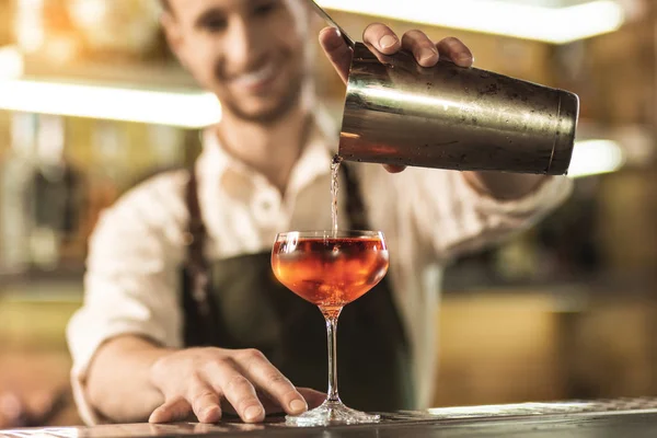 Angenehmer junger Mann gießt Cocktail aus Shaker — Stockfoto