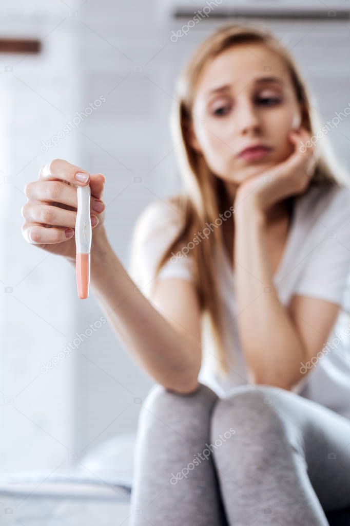 Low-spirited woman holding her pregnancy test