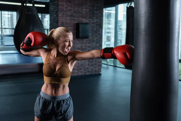 Blonde-haired female boxer having nice abs boxing hard