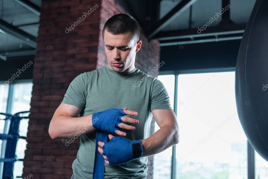 Dark-haired boxer using wrist wraps in gym