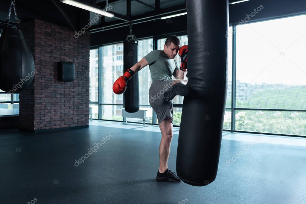 Dark-haired boxer beating punching bag with leg
