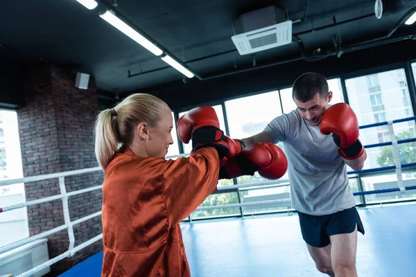 Deportista de pelo oscuro boxeando activamente con su entrenador femenino — Foto de Stock
