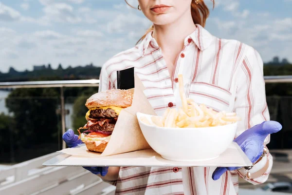 Camarera joven sosteniendo hamburguesa y patatas fritas para los clientes — Foto de Stock