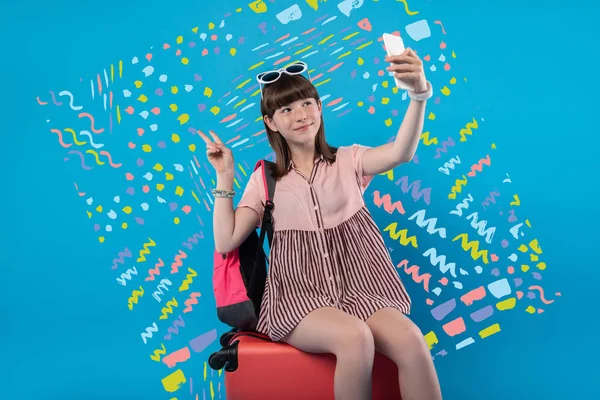 Happy girl taking a selfie while sitting on a suitcase — Stock Photo, Image