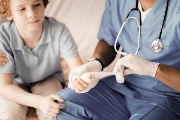 Frustrated kid putting his hand on the knees of his doctor — Stock Photo, Image