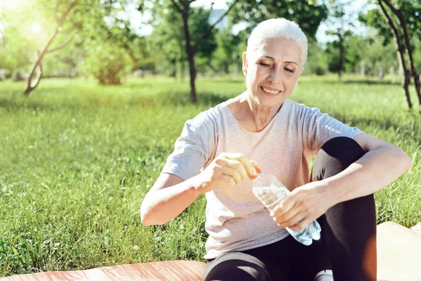 Relaxing smiling pensioner drinking water in a park