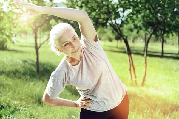 Serious calm pensioner slowly doing the exercises