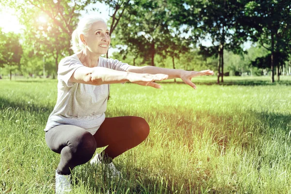 Äldre kvinna böjer knä i en park — Stockfoto