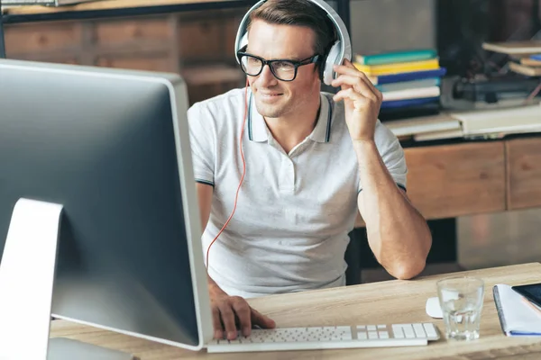 Positiver intelligenter Mann, der seine Kopfhörer berührt — Stockfoto