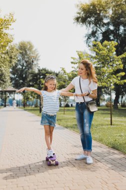 Şık modern anne ve kızı kaykay ile yürüyüş