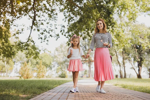 Linda chica hermosa con piruleta en la mano caminando con la madre —  Fotos de Stock