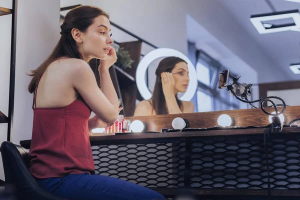 Dark-haired beauty blogger sitting near her makeup table