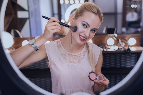 Blauwogige vrouw die lacht tijdens haar make-up op te zetten — Stockfoto