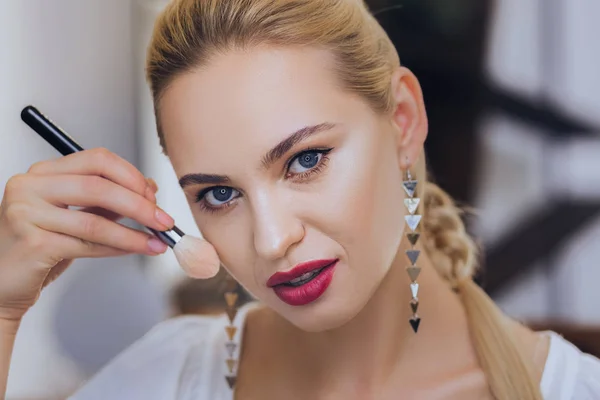 Mujer de ojos azules de pie frente al espejo con cepillo de maquillaje — Foto de Stock