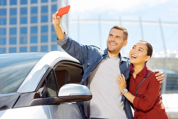 Encantada pareja positiva mirando en la cámara del teléfono inteligente — Foto de Stock