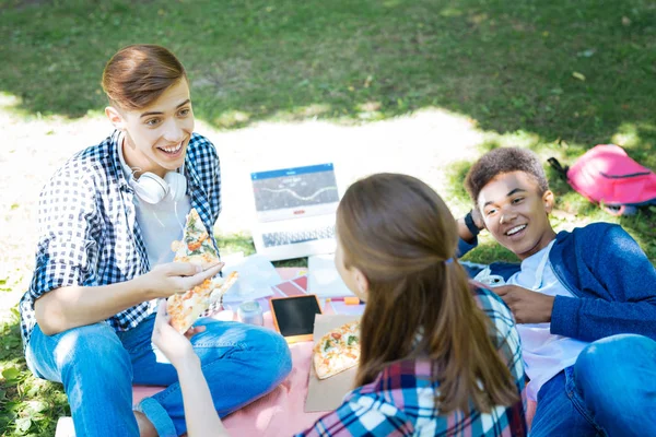 Tres estudiantes activos tomando un descanso para comer pizza mientras trabajan en el proyecto —  Fotos de Stock