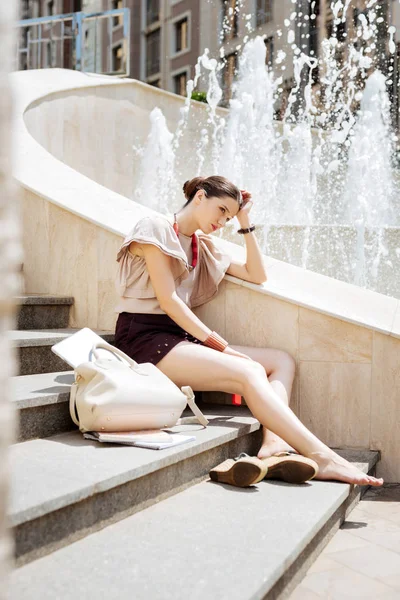 Приятная молодая женщина сидит у фонтана — стоковое фото