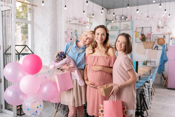 Two beautiful women standing near their pregnant sister with presents