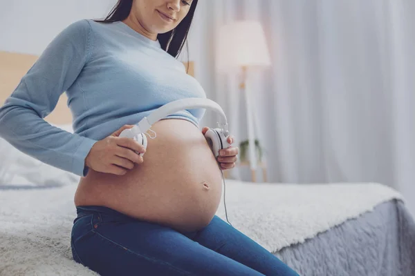 Brünette setzt sich Kopfhörer auf Bauch — Stockfoto