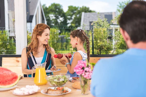 Pleasant nice girl offering ketchup to her mother — Stock Photo, Image