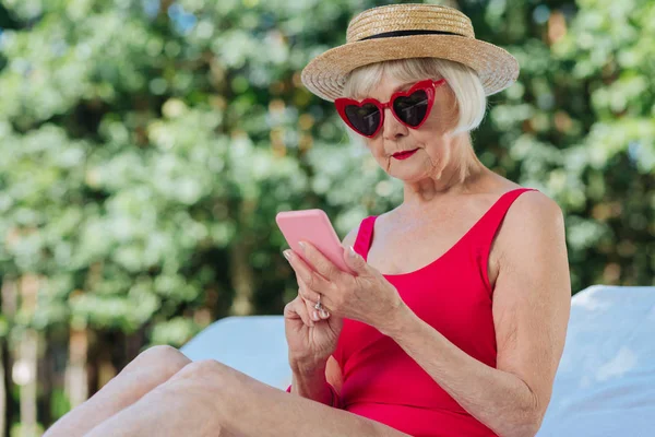 Femme mature moderne tenant son téléphone intelligent rose dans les mains — Photo