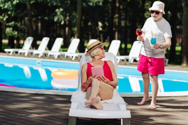 Retired man wearing red shorts bringing cocktails his wife