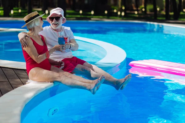 Radiante aposentados felizes sentados perto de grande piscina exterior — Fotografia de Stock