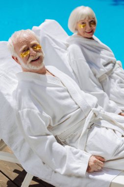 Emekliler göz yamaları ve havuz yalan beyaz bornoz giyiyor