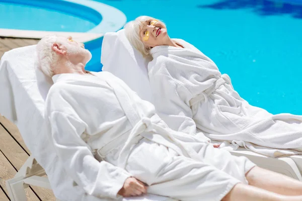 Homme et femme retraités portant des peignoirs blancs refroidissant près de la piscine — Photo