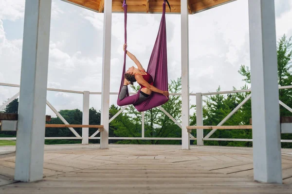 Aerial yoga. Beautiful woman with nice body and abs feeling calm and rested while practicing aerial yoga