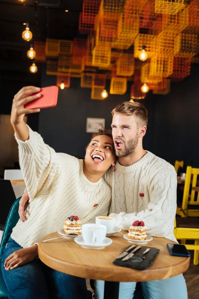 Divertida linda pareja haciendo foto memorable sentado en la cafetería —  Fotos de Stock