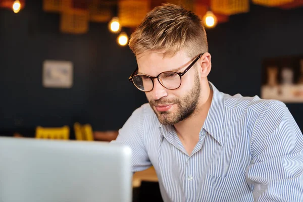 Homem de cabelos loiros barbudo usando óculos olhando para seu laptop — Fotografia de Stock