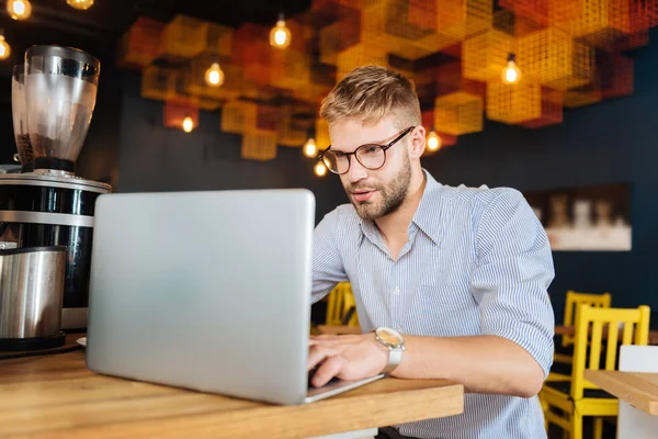 Hardworking blonde-haired man typing some information on laptop