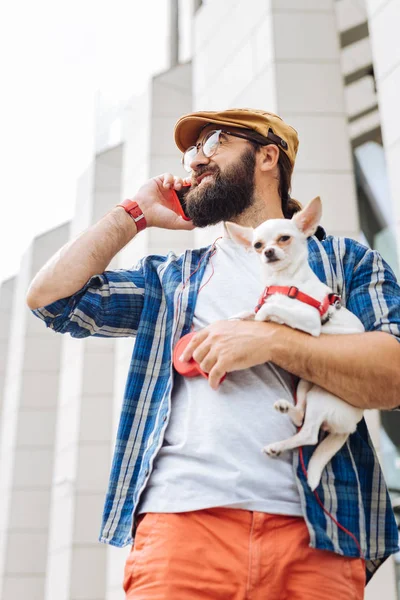 Küçük beyaz bir köpek ile şehir yürüyen esmer adam