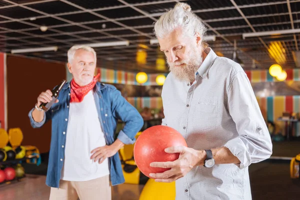 Homem idoso agradável olhando para a bola de boliche — Fotografia de Stock