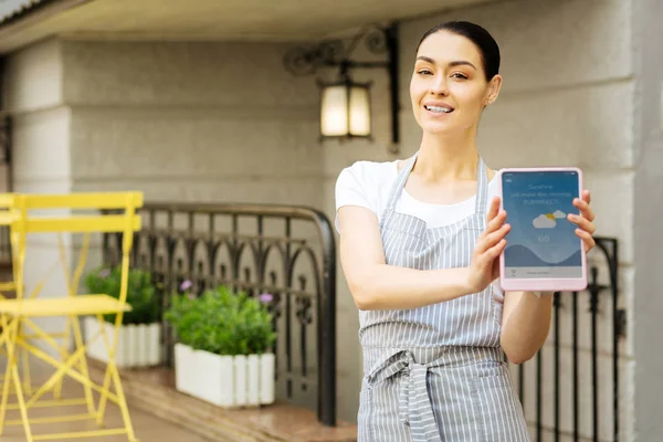 Улыбающаяся официантка стоит на улице и держит планшет — стоковое фото