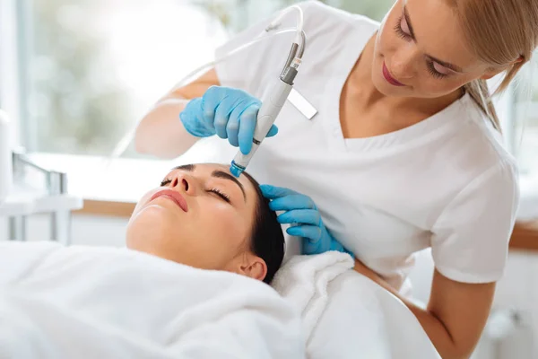 Smart nice cosmetologist looking at the clients face — Stock Photo, Image