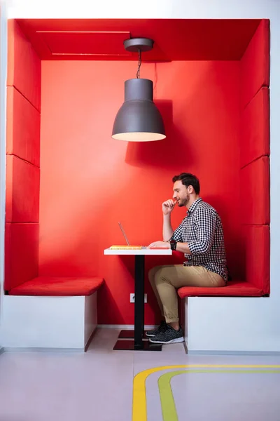 Jonge man zitten in de futuristische rode ruimte en die op laptop werkt — Stockfoto