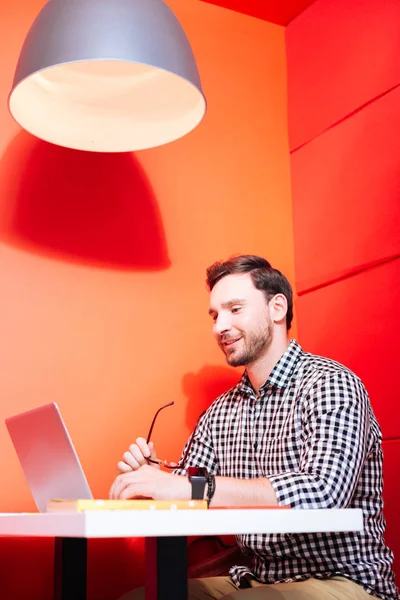 Knappe man glimlachend en bezig met zijn handige moderne laptop — Stockfoto