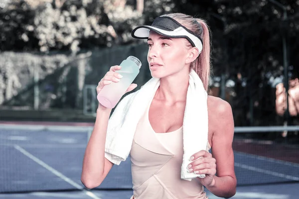 Nachdenkliche Spielerin trinkt nach dem Tennis Wasser — Stockfoto