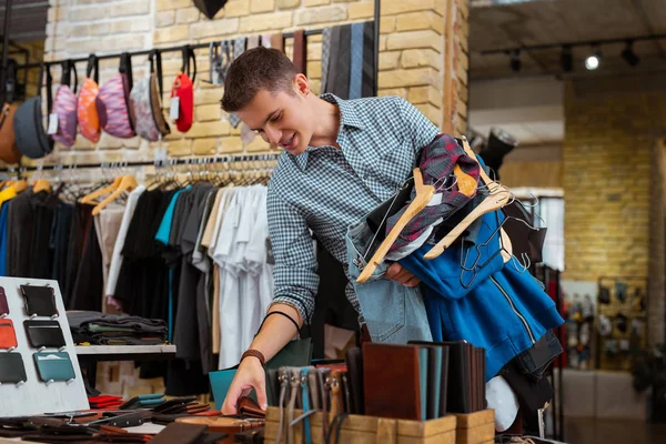 Munter mand læner sig til bordet i tøjbutik og ser på tegnebøger - Stock-foto