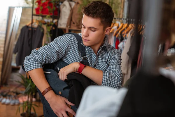 Careful young man stealing black T shirt while being in clothes shop — Stock Photo, Image
