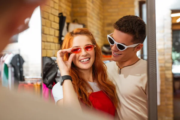 Adorable girl wearing red glasses and her boyfriend looking at her — Stock Photo, Image