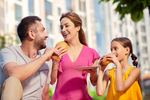 Família feliz alegre comendo hambúrgueres muito saborosos — Fotografia de Stock