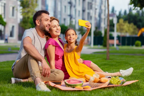 Family selfie. Joyful pretty girl holding her smartphone while taking a selfie together with family